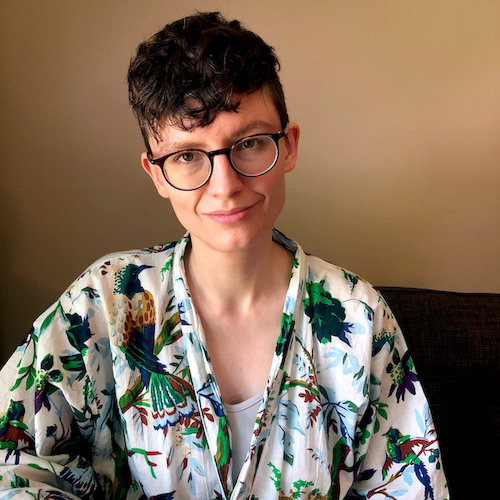 A white person with short curly brown hair and glasses wearing a robe covered in colorful tropical birds and flowers.